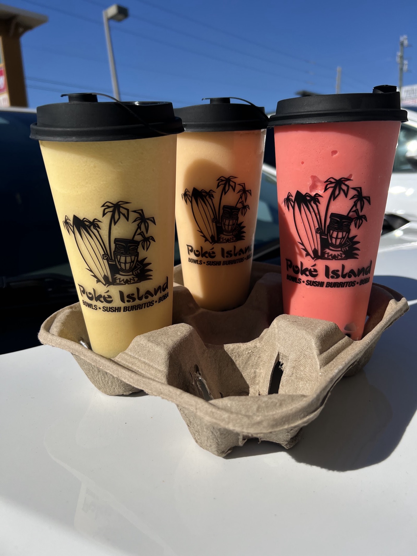 Three Poké Island boba drinks in a carry tray: a yellow, a tan and a pink blended smoothie.