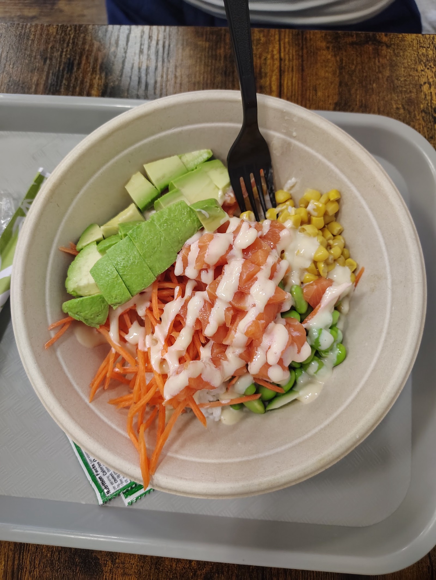 A poke bowl with salmon, avocado, shredded carrot, sweet corn and edamame over rice, finished with a creamy drizzle.