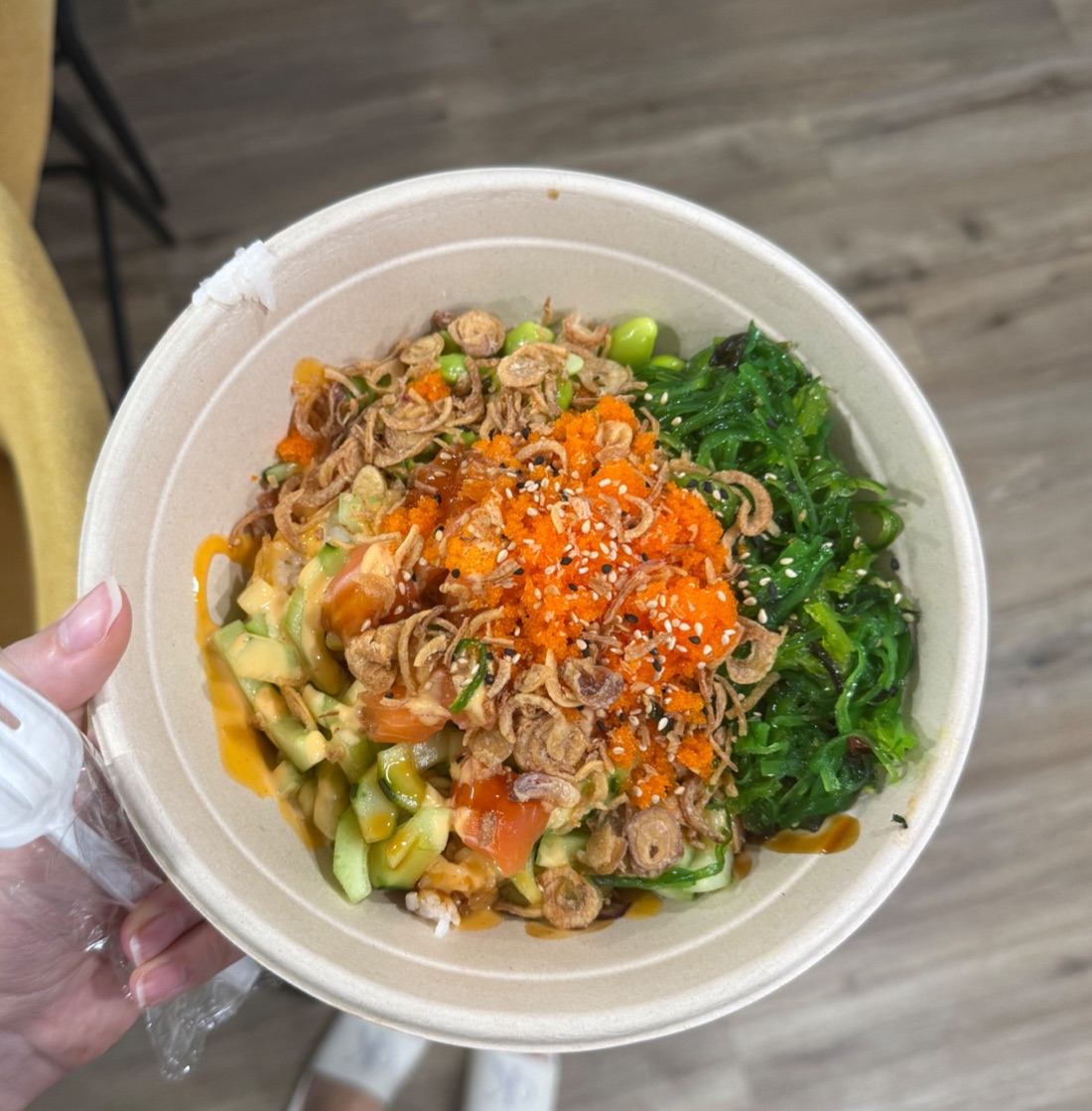 A poke bowl topped with orange tobiko, seaweed salad, cucumber, tomato and crispy fried shallots.
